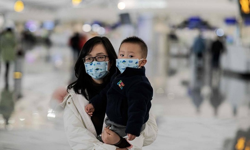 Uma mulher com uma criança no colo usa máscaras de proteção no aeroporto internacional de Daxing, em Pequim. Número de mortes causadas pelo coronavírus na China chegou a 17 nesta quarta-feira Foto: NICOLAS ASFOURI / AFP 