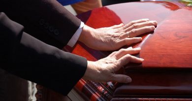 2 hands touching a closed wooden casket.  Farewell to a loved one.