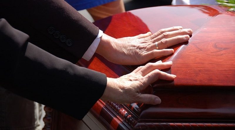 2 hands touching a closed wooden casket.  Farewell to a loved one.