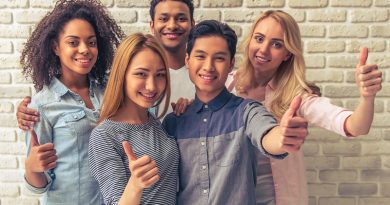 Portrait of beautiful young people of different nationalities showing Ok signs, looking at camera and smiling, against white brick wall