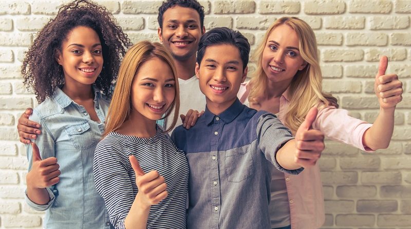 Portrait of beautiful young people of different nationalities showing Ok signs, looking at camera and smiling, against white brick wall