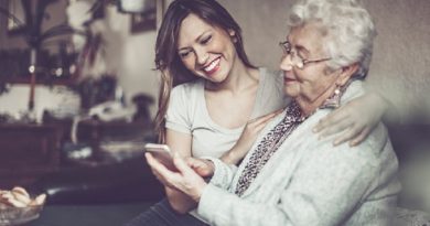 Social worker is visiting a senior woman in her own apartment. They are celebrating the elderly lady's birthday. The kind nurse is hugging the senior woman over her shoulder.