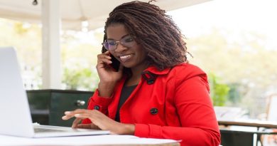 Cheerful woman using laptop and smartphone. Attractive young businesswoman talking by cell phone and using laptop computer in outdoor cafe. Remote work concept