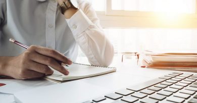 Close up young business woman sitting at table and taking notes in notebook on table is laptop and many books. Student learning online. Blogger.