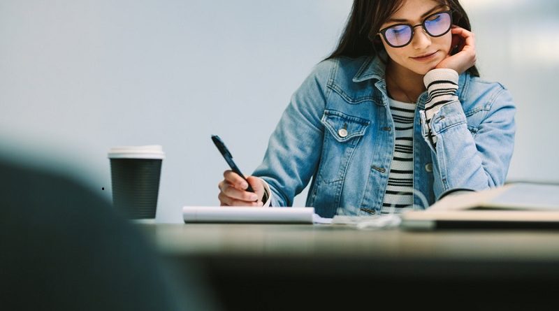 Happy female student sitting at college library and making notes. Woman studying at university library.