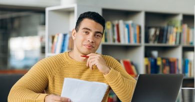 Portrait of young adult hispanic male freelancer or student is looking at the camera with smile. Attractive business man sits at the work desk, making notes, learning online
