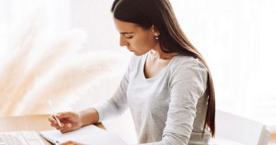 A beautiful student girl is sitting at a desk and making notes in a notebook, using a laptop to prepare for classes. Modern technologies, online education, training.
