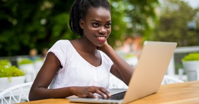 Young black curly female is sitting in street bar and having remote work using laptop