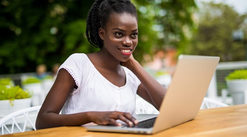 Young black curly female is sitting in street bar and having remote work using laptop