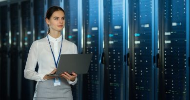 Beautiful Data Center Female IT Technician Walking Through Server Rack Corridor with a Laptop Computer. She is Visually Inspecting Working Server Cabinets.