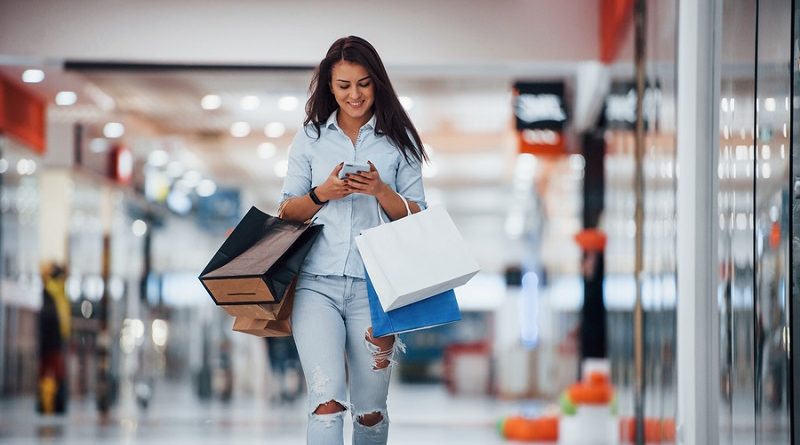 Brunette woman in the supermarket with many of packages and phone in hands have shopping day.