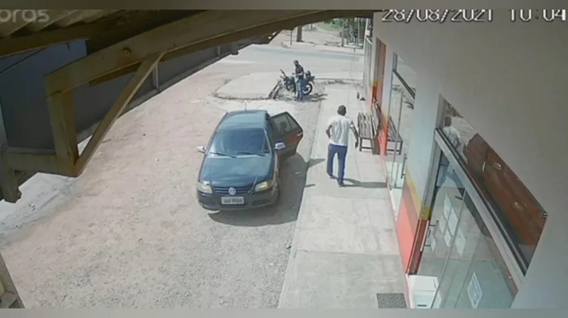 Condutor da moto (de camisa preta) se prepara para dar fuga ao homem (de camisa branca) que deu tiro em soldado — Foto: Circuito de segurança/Reprodução