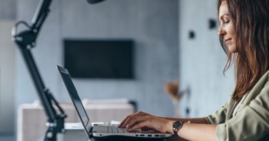 Woman works at home sitting at her desk with her laptop. Side view.