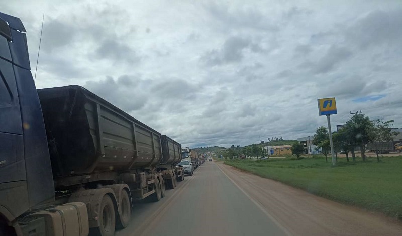 Caminhões trafegam lentamente pela rodovia esburacada. 