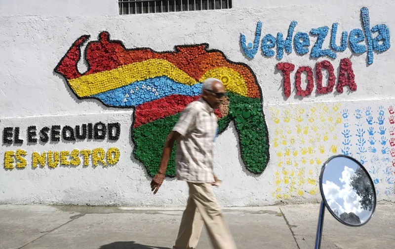 Homem caminha diante de muro com mensagem reivindicado a região guianesa de Essequibo como venezuelana, em Caracas, em 29 de novembro de 2023. — Foto: Matias Delacroix/ AP