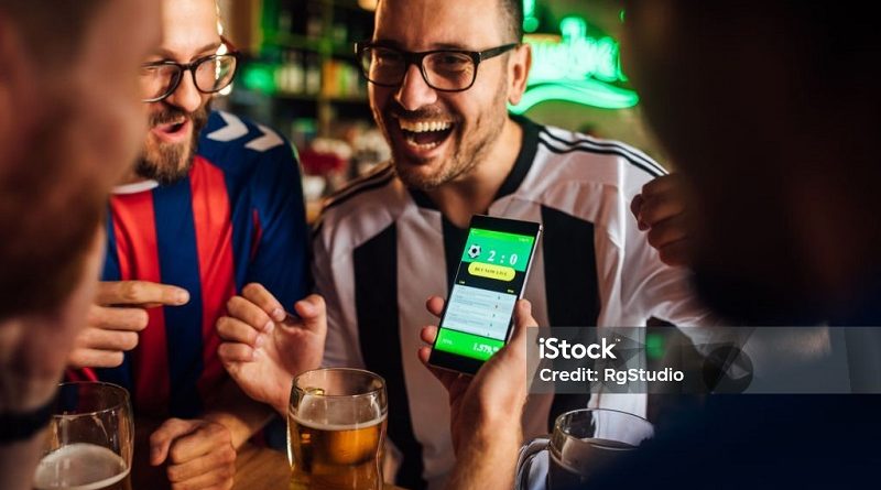 Soccer fans drinking beer at the pub and using mobile app for betting.